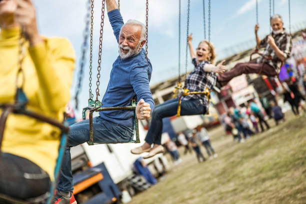 istock Happy senior friends having fun while riding on chain swing at amusement park. 1324999416