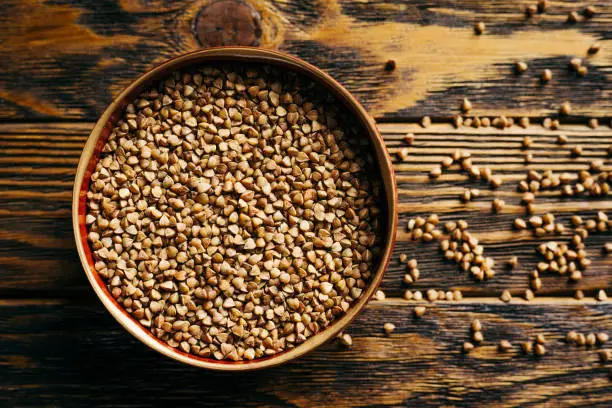 Photo of raw buckwheat in a bowl on a wooden background, top view