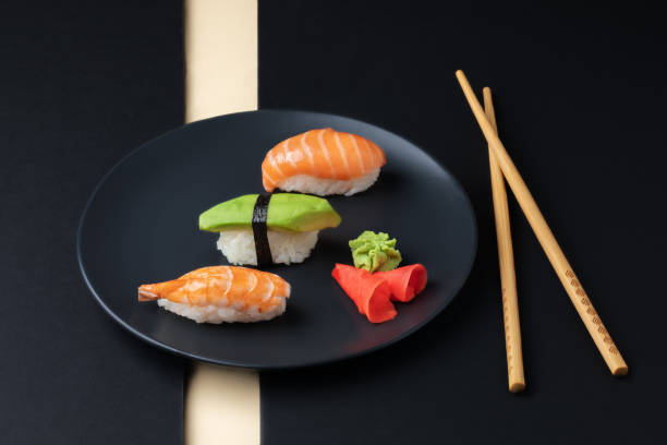 Japanese cuisine - set of nigiri sushi with salmon, avocado ans schrimp on a black plate with chopsticks. stock photo