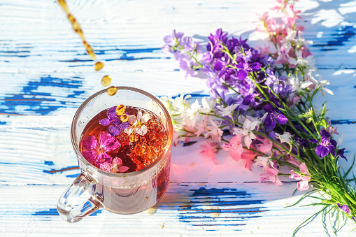 Transparent glass cup of tea with wildflowers and a bouquet on a wooden table close-up. Summer lifestyle concept. Selective focus
