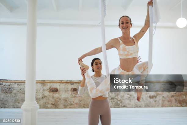 An Aerial Yogainstructor Helping A Pupil Stock Photo - Download Image Now - Aerial Yoga, Yoga, 25-29 Years