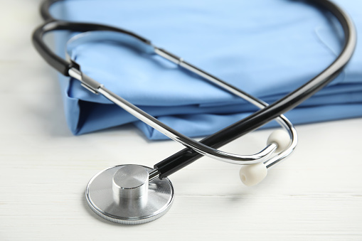 Stethoscope and medical uniform on white wooden background, closeup