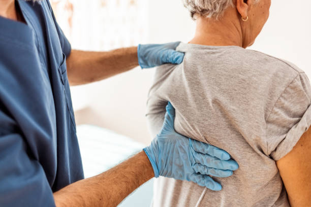 Back pain medical examination. Senior adult, female patient does arm exercises with her home healthcare male nurse or physical therapist in nursing home. disk stock pictures, royalty-free photos & images