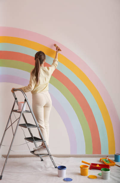 mujer joven pintando arco iris en la pared blanca en el interior, vista trasera - female house painter home decorator paintbrush fotografías e imágenes de stock