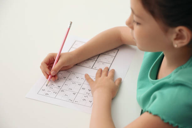 kleines mädchen, das sudoku-rätsel am weißen tisch löst, nahaufnahme - child thinking writing little girls stock-fotos und bilder