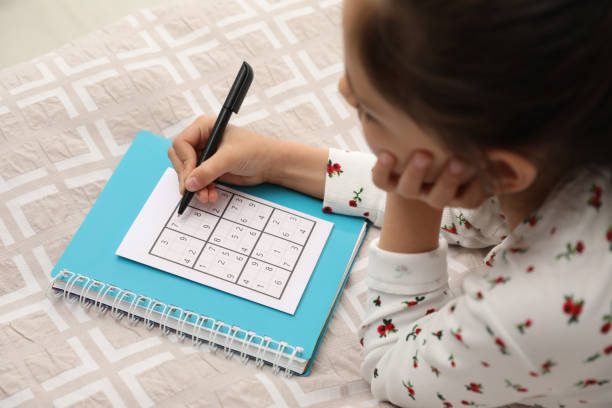 kleines mädchen, das sudoku-rätsel auf dem bett löst - child thinking writing little girls stock-fotos und bilder