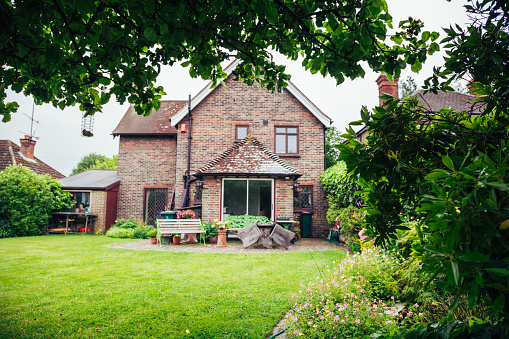 Color image depicting the exterior of a traditional detached English house in the countryside, with a freshly manicured lawn and garden. Room for copy space.