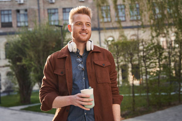 istock Man wearing headphones looking away and drinking coffee 1325023077