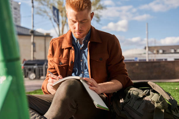 istock Concentrated ginger man sitting at the parapet and writing something 1325023566
