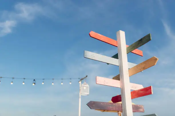 Guidepost with bright colored arrows in the sunlight with blue sky background.