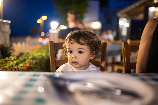 Hungry little boy waiting for a dinner at outdoor restaurant during summer vacation
