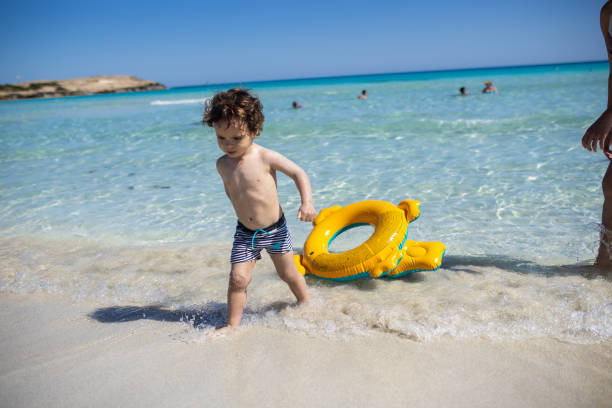 Happy little boy having fun in sea during beach holiday, during coronavirus pandemic after reopening borders