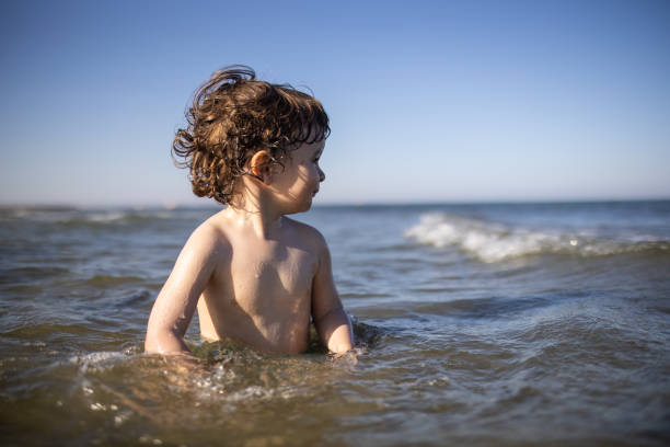 Happy little boy having fun in sea during beach holiday, during coronavirus pandemic after reopening borders