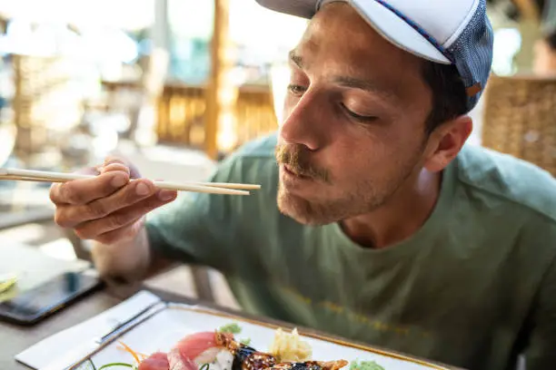 Young man eating delicious sushi with chopsticks at outdoor restaurant. Sashimi, nigiri, unagi sushi, tuna, salmon, wasabi
