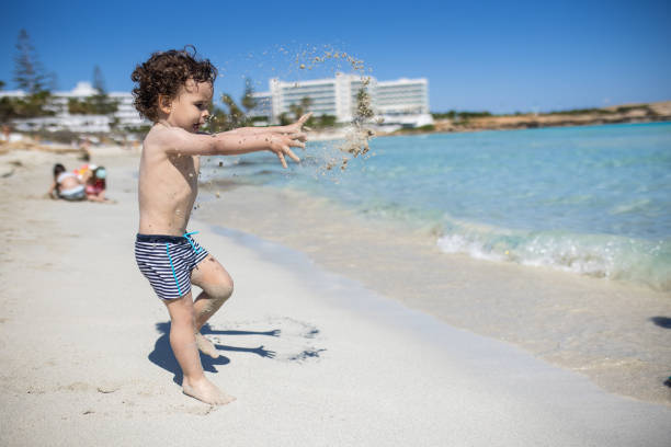 Toddler throwing sand while playing on beach during summer vacation, during coronavirus pandemic after reopening borders