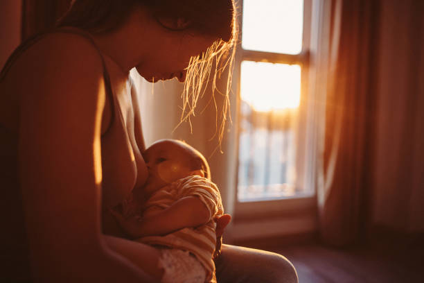 Two people, mother breastfeeding her baby boy son in sunset at home.