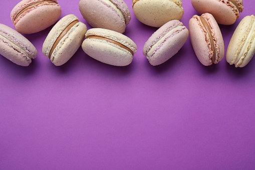 Delicious colorful macarons on purple background, flat lay. Space for text