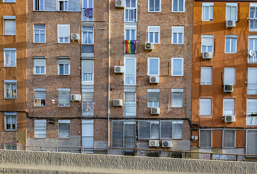 Front view of brick facade with balconies and windows of a block of flats in a suburban area. An lgbtqia flag hangs from one of the windows