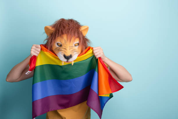 istock Young woman in lion mask aggressively biting rainbow pride lgbt flag while holding it with two hands 1325035691