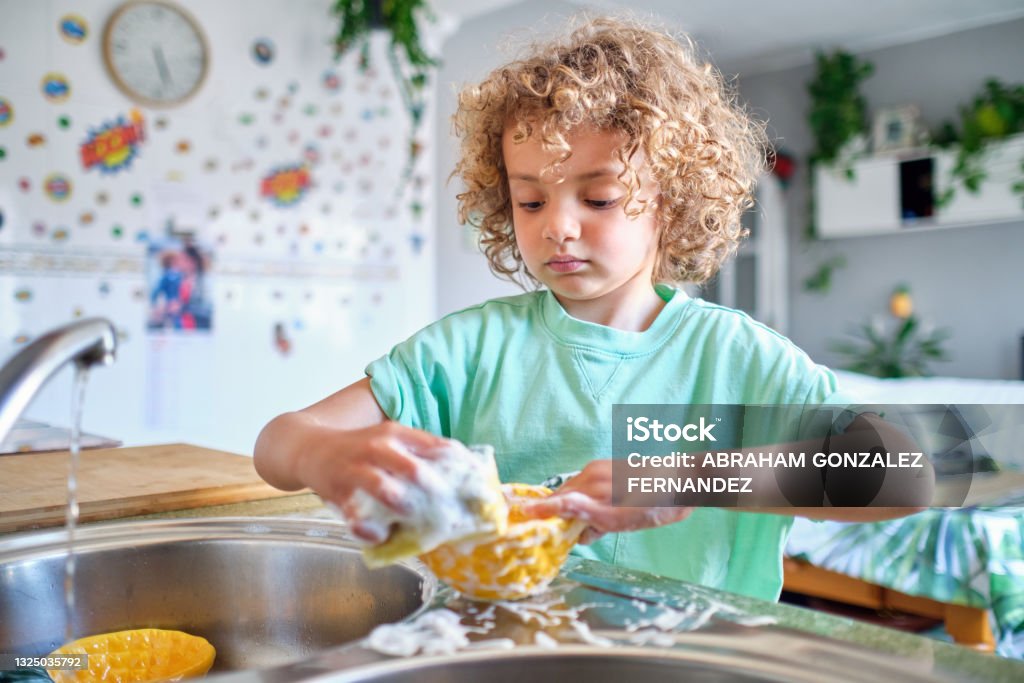 hispanic child washing lunch dishes with soap and water Child Stock Photo
