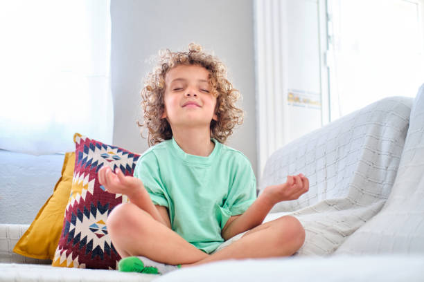 niño practicando la meditación sentado en el sofá de casa en pose de loto - gente tranquila fotografías e imágenes de stock