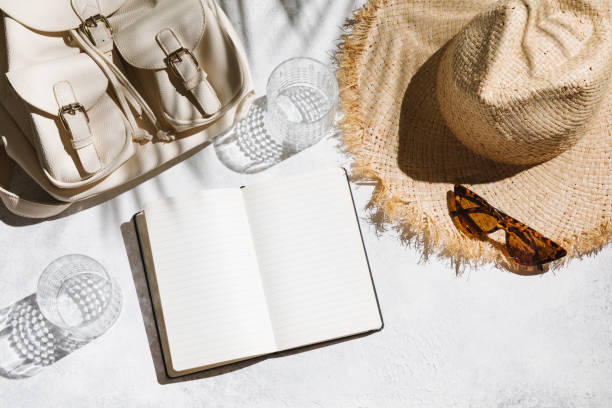 Summer holiday concept. Travel flat lay with notepad, backpack, and hat on white table background. stock photo