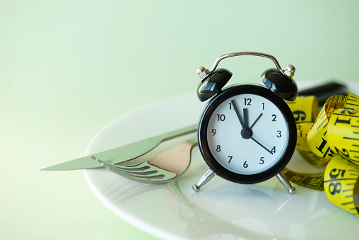 Measuring tape in empty plate with alarm clock, fork and spoon.