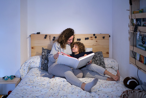 young woman reading a story to her son lying in bed