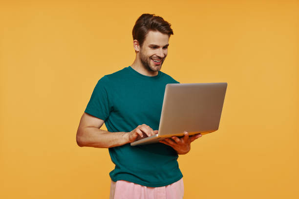 istock Handsome young man in casual clothing using laptop and smiling 1325049528