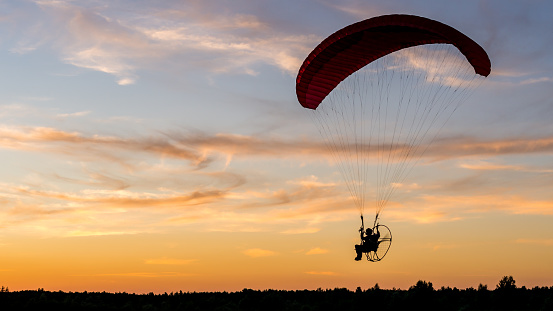 Powered paragliding pilot silhouette with back-mounted motor (paramotor) during sunset.