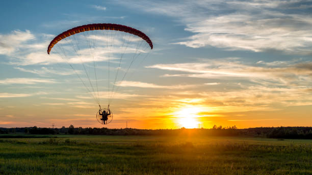 istock Beautiful landscape with back view of paramotor pilot over rural meadow during sunset 1325054550