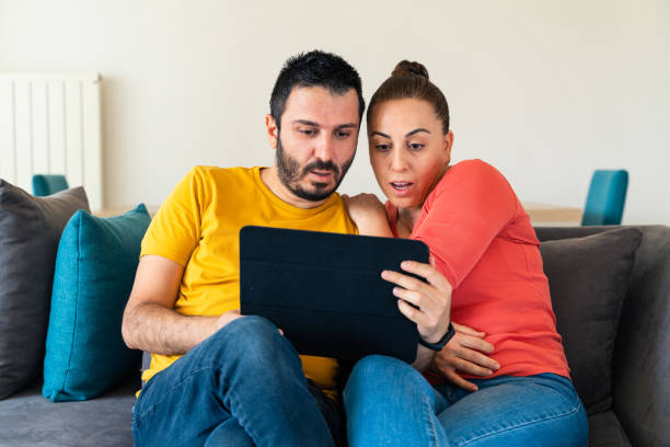 jeune couple surpris regardant un film sur tablette numérique - women computer couple surprise photos et images de collection