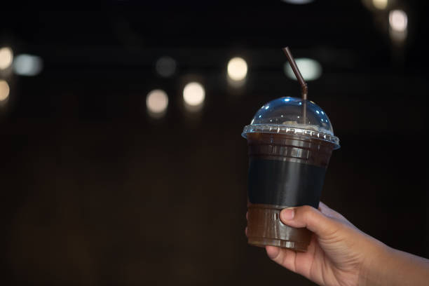 hand holding plastic cup of iced black coffee with blurry light of coffee shop background - black coffee coffee single object drink imagens e fotografias de stock