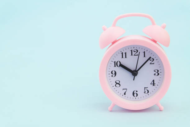 istock Pink alarm clock on blue background 1325062090