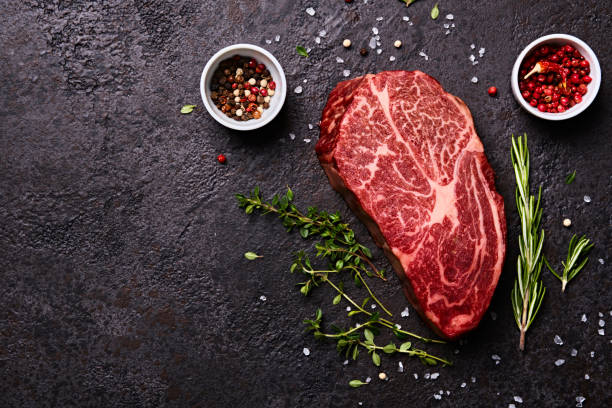 istock Fresh raw marbled beef rib eye steak and spices on black stone background, copy space 1325062159