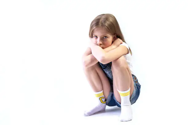 Photo of Teenage girl in denim overalls squatting on white background