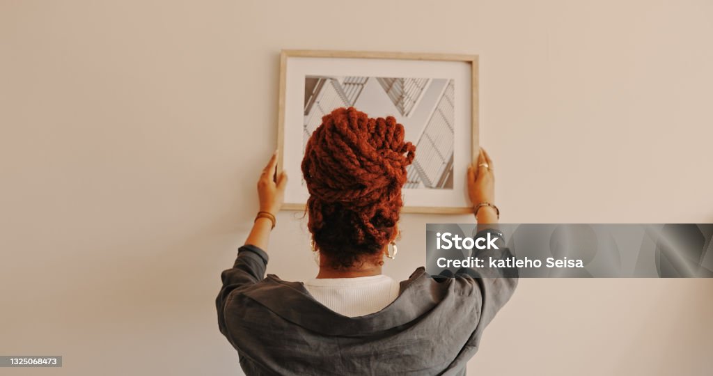 Shot of a unrecognizable female hanging a painting at home That looks like the right spot Hanging Stock Photo