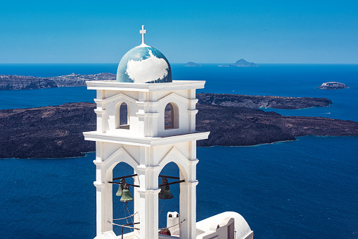 A typical white belltower of an old church/chapel with a small dome in the picturesque old town of Imerovigli village. In the background the famous Santorini caldera, which is for a big part under the sea leval. Location: Santorini island, Greece.