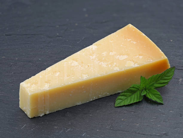 one piece of parmigiano cheese on slate plate, parmesan with green leaf one piece of parmigiano cheese on slate plate, parmesan with green leaf. grana padano stock pictures, royalty-free photos & images