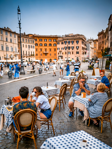 Rome, Italy, June 19 -- Some tourists enjoy life and an Italian-style breakfast sitting in a sidewalk cafe in Piazza Navona, in the historic and baroque heart of Rome. Piazza Navona is much loved by tourists and residents for the presence of numerous typical restaurants and for the monumental and artistic treasures of one of the most famous squares in the world. Image in high definition format.