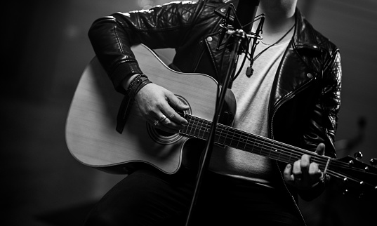 Photo of man playing acoustic guitar. Man sitting at studio microphone. Music, arts and entertainment concept.