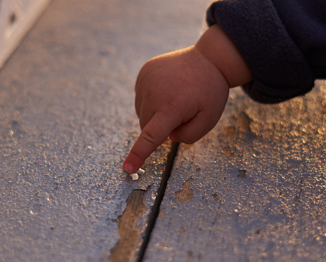 A young child's hand pointing at something on a wood board with chipped paint at a playground at dusk under sunset in Calgary, Alberta, Canada in a spring evening