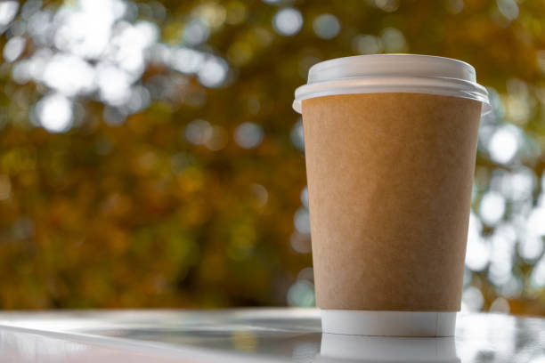 istock Paper disposable coffee cup on a white table with autumn bokeh. 1325082428