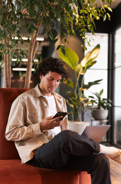 istock Young man online with mobile phone in open plan office renting work space for start up business 1325083429