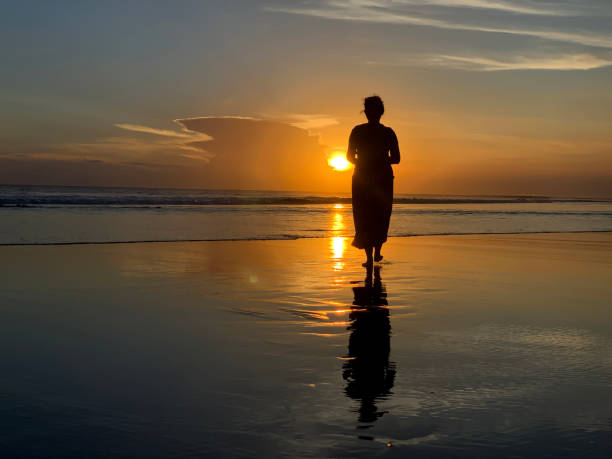silueta de una mujer caminando por la playa con los pies descalzos al atardecer. - one person beautiful barefoot beach fotografías e imágenes de stock