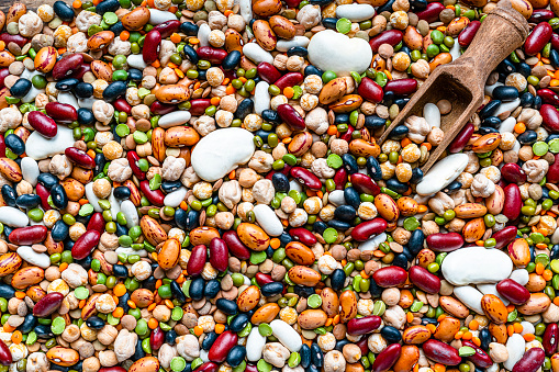 Close up view of a large collection of dried legumes and beans shot from above. A wooden serving scoop complete the composition
