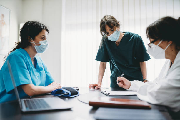 una doctora está teniendo una reunión con dos enfermeras en una clínica médica - discussion talking italy usa fotografías e imágenes de stock