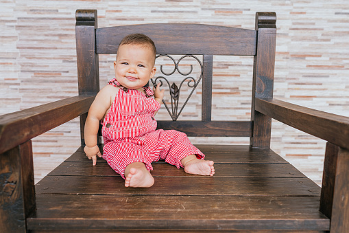 Beautiful baby sitting in a wooden chair on the terrace making funny faces.