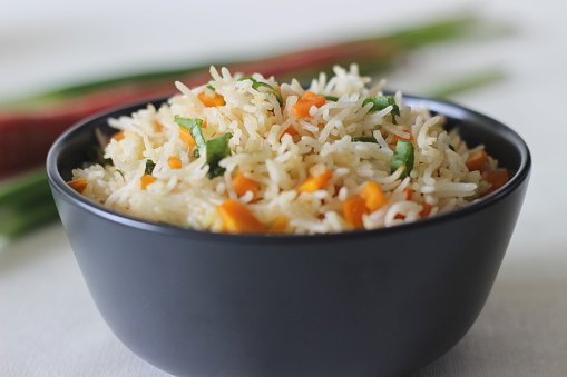 Vegetable Carrot Fried Rice with Indian spices. Shot on white back ground along with carrots and spring onions