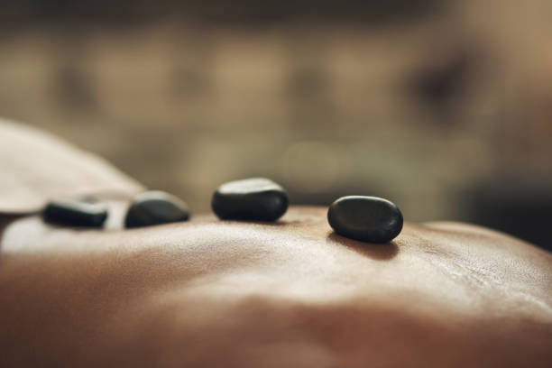 foto recortada de un hombre recibiendo un masaje con piedras calientes en un spa - massage stones fotografías e imágenes de stock